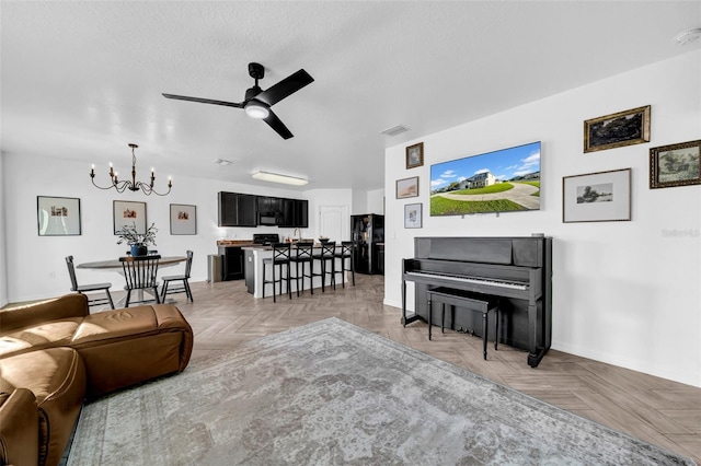 living area with ceiling fan with notable chandelier, a textured ceiling, and visible vents