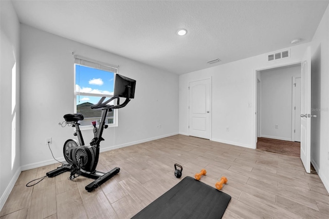 workout room featuring visible vents, light wood-style flooring, baseboards, and a textured ceiling