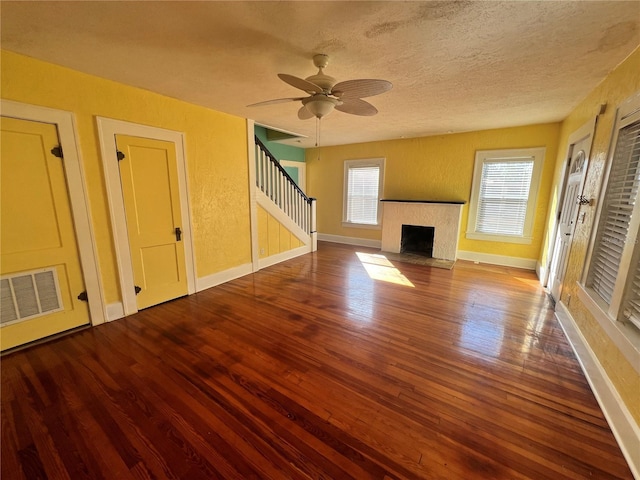 unfurnished living room with baseboards, visible vents, a fireplace with flush hearth, wood finished floors, and stairs