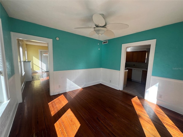 unfurnished room featuring a ceiling fan, a wainscoted wall, visible vents, and wood finished floors