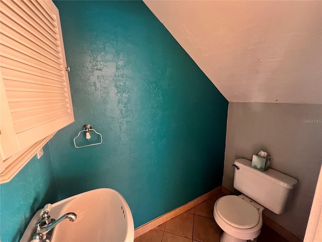 bathroom with toilet, a sink, baseboards, vaulted ceiling, and tile patterned floors