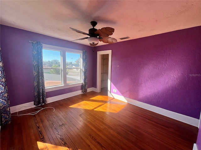 unfurnished room featuring visible vents, a textured wall, a ceiling fan, wood finished floors, and baseboards