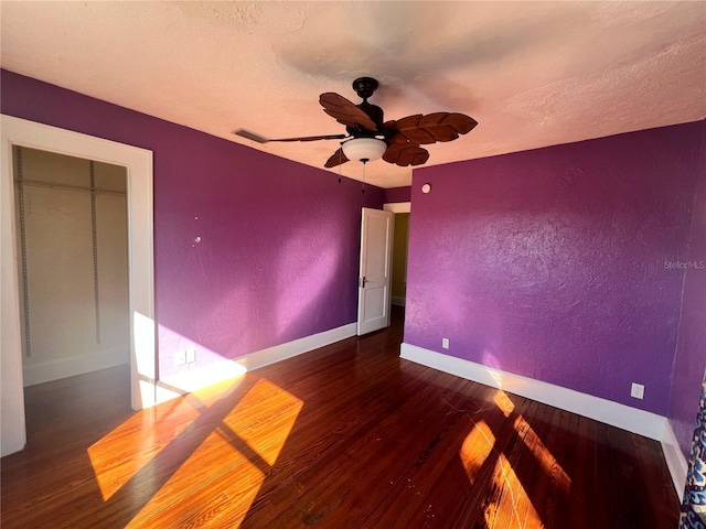 unfurnished bedroom with dark wood-type flooring, visible vents, a textured wall, and baseboards