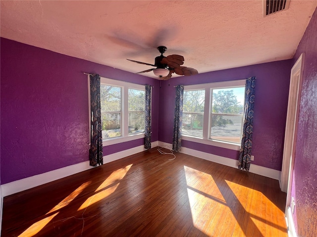 unfurnished room featuring a textured ceiling, a textured wall, wood finished floors, visible vents, and baseboards