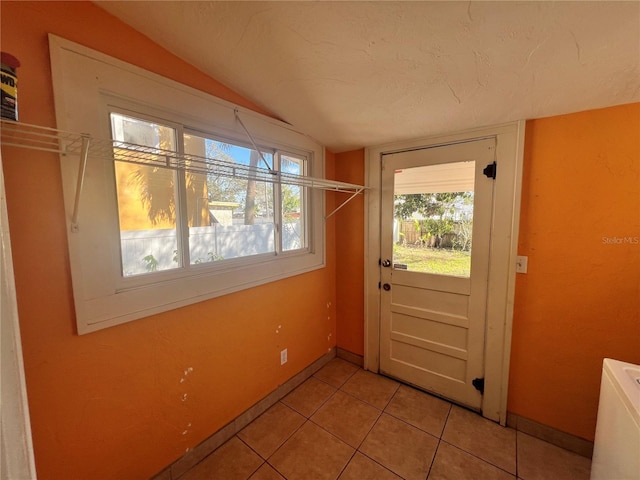 entryway with vaulted ceiling, a textured ceiling, baseboards, and light tile patterned floors