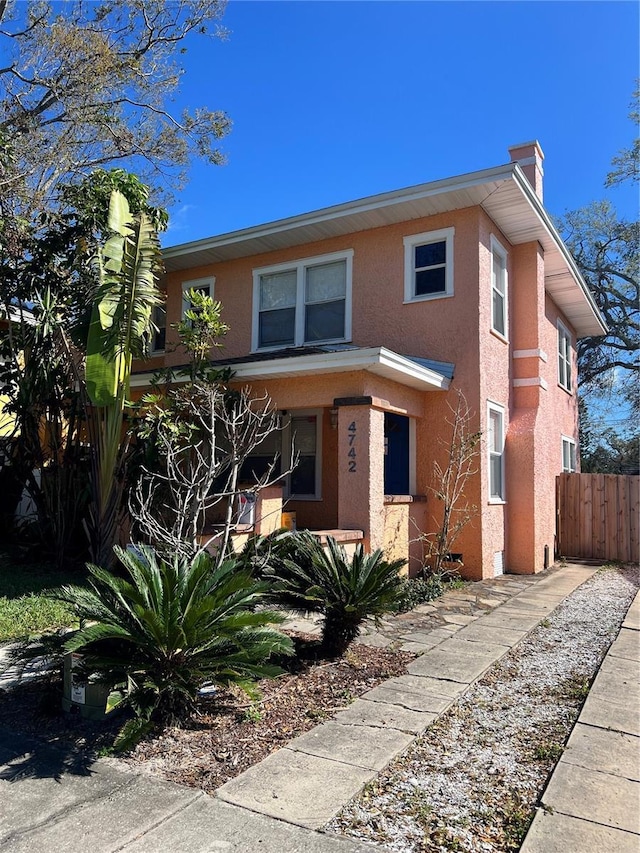 view of front facade featuring a chimney, fence, and stucco siding