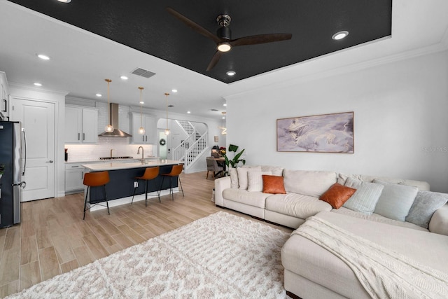 living room featuring visible vents, stairway, ornamental molding, a tray ceiling, and light wood-style floors