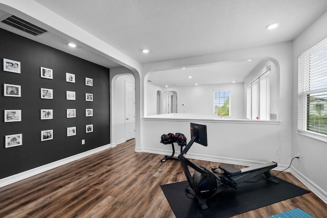 workout area with baseboards, visible vents, arched walkways, and dark wood-type flooring