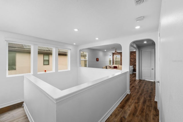 corridor with arched walkways, visible vents, and wood finished floors