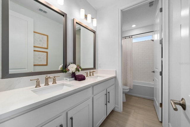 bathroom with toilet, double vanity, a sink, and visible vents