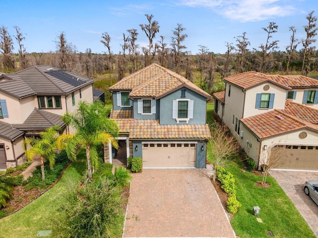 view of front of property with a tiled roof, an attached garage, decorative driveway, a front lawn, and stucco siding