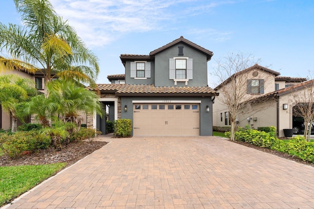 mediterranean / spanish home featuring decorative driveway, a tiled roof, an attached garage, and stucco siding