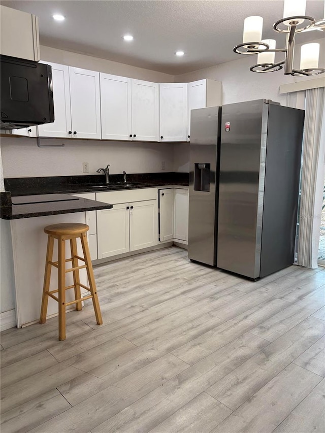 kitchen featuring light wood finished floors, stainless steel fridge with ice dispenser, dark countertops, white cabinetry, and a sink