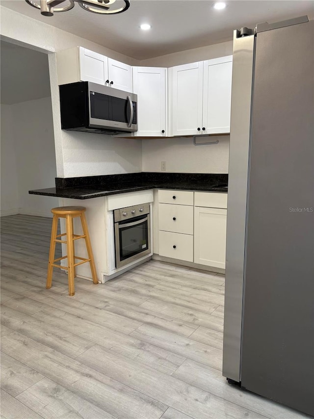 kitchen with a kitchen breakfast bar, appliances with stainless steel finishes, white cabinetry, and light wood-style floors