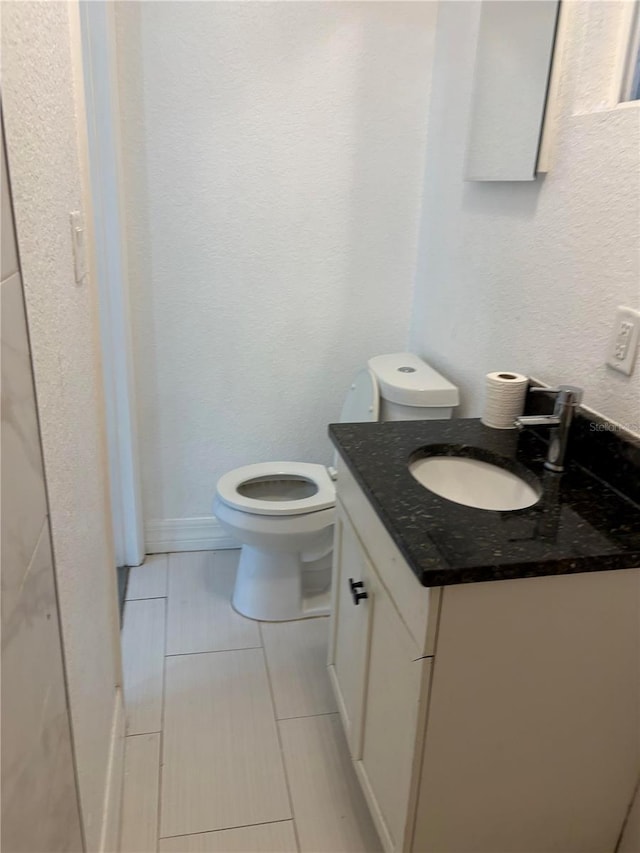 half bath featuring a textured wall, vanity, and toilet