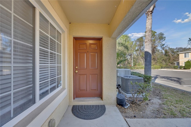 view of exterior entry featuring central air condition unit and stucco siding