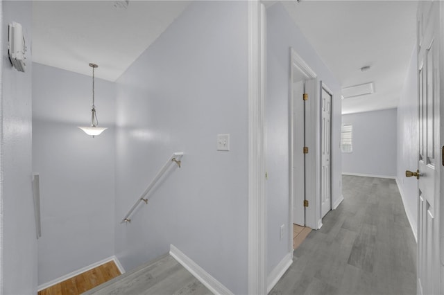 hallway featuring attic access, baseboards, wood finished floors, and an upstairs landing