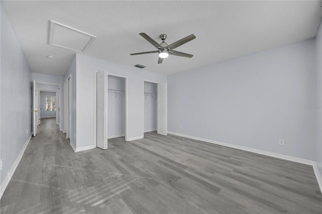 unfurnished bedroom featuring two closets, visible vents, attic access, wood finished floors, and baseboards