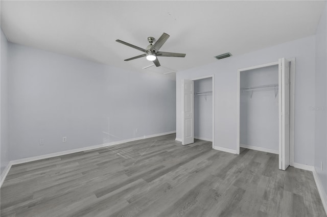 unfurnished bedroom featuring baseboards, visible vents, two closets, and wood finished floors