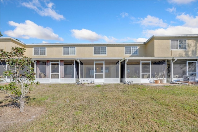 rear view of property with a yard, a sunroom, and stucco siding