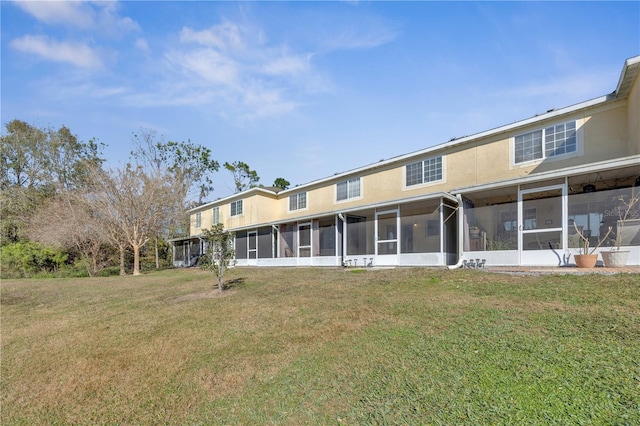 rear view of property featuring a sunroom, a yard, and stucco siding