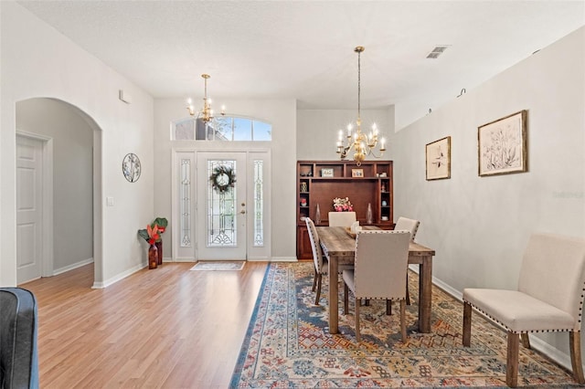 dining space with arched walkways, a notable chandelier, visible vents, baseboards, and light wood-type flooring