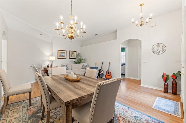 dining area featuring a chandelier, arched walkways, light wood-style flooring, and baseboards