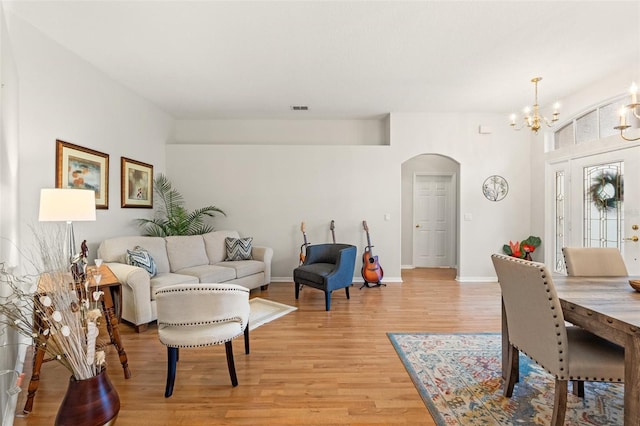 living area with visible vents, arched walkways, baseboards, light wood-style flooring, and a notable chandelier