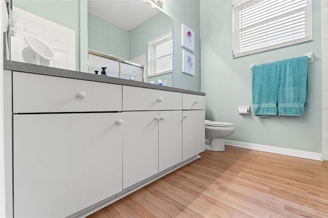 full bath with baseboards, toilet, a shower with door, wood finished floors, and vanity