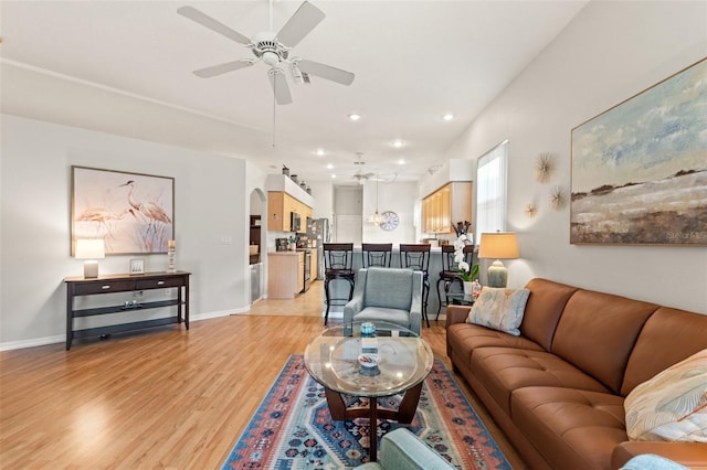 living area with arched walkways, ceiling fan, light wood-style flooring, and baseboards