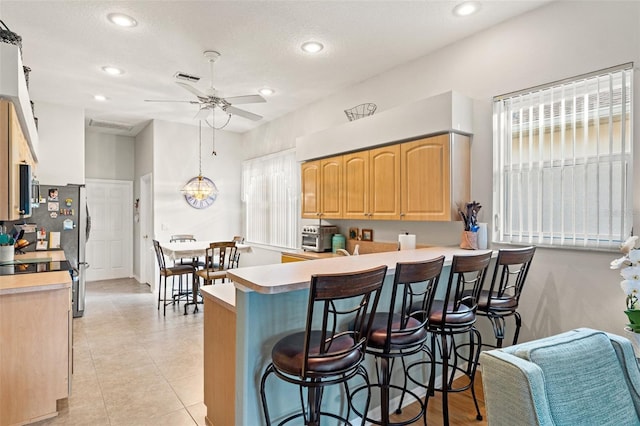 kitchen with light brown cabinetry, light countertops, a kitchen bar, and visible vents