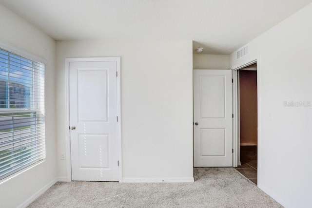 unfurnished bedroom with light colored carpet, visible vents, baseboards, and multiple windows