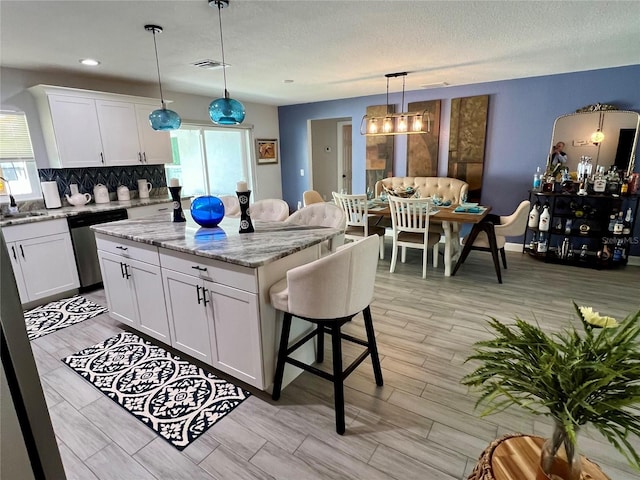 kitchen with white cabinetry, a sink, dishwasher, tasteful backsplash, and a center island