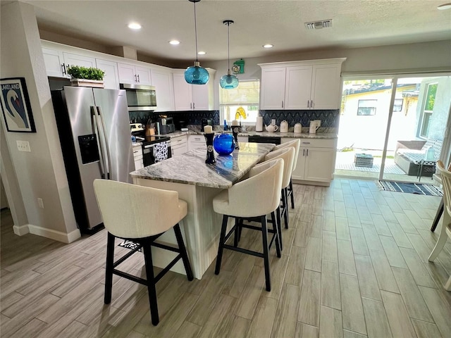 kitchen featuring visible vents, wood finish floors, a kitchen island, stainless steel appliances, and decorative backsplash