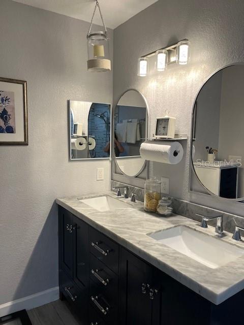 full bathroom with a sink, baseboards, double vanity, and a textured wall