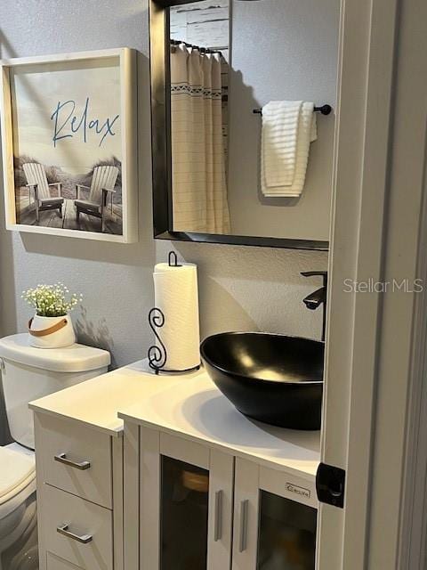 full bath with toilet, vanity, and a textured wall