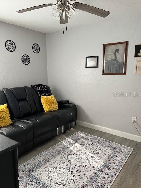 living room with baseboards, ceiling fan, and wood finished floors