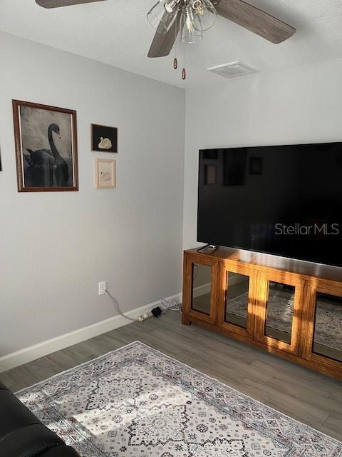 living area with wood finished floors, a ceiling fan, baseboards, and visible vents