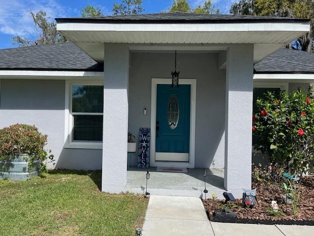 entrance to property with stucco siding, a shingled roof, and a yard