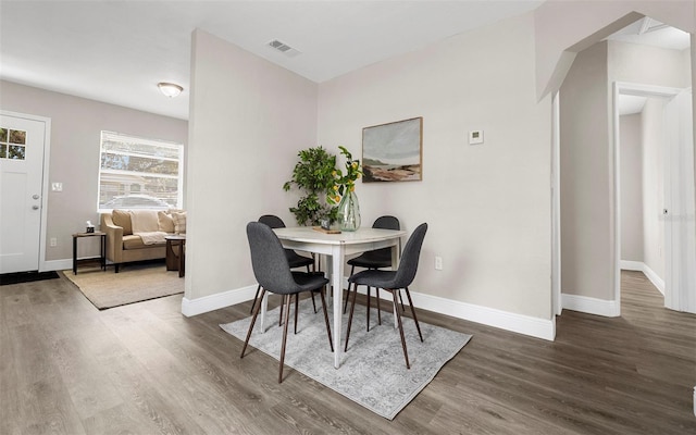 dining room with arched walkways, visible vents, baseboards, and wood finished floors