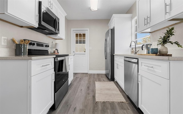 kitchen featuring appliances with stainless steel finishes, white cabinetry, a sink, wood finished floors, and baseboards