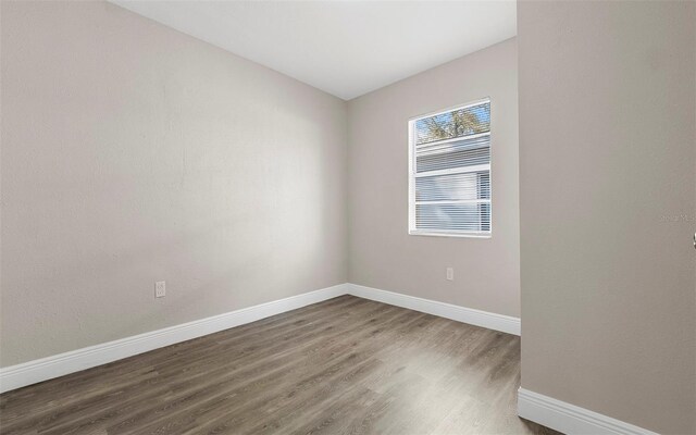 spare room with baseboards and wood finished floors