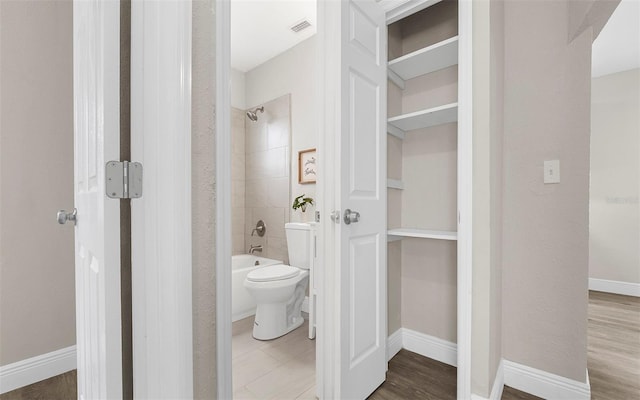 bathroom featuring baseboards, visible vents, toilet, wood finished floors, and  shower combination