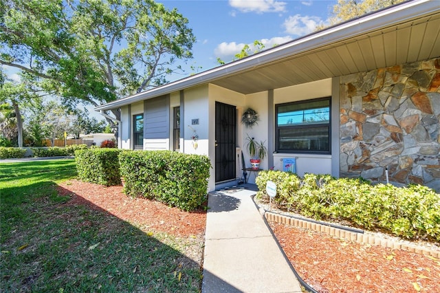 entrance to property with stone siding and a lawn