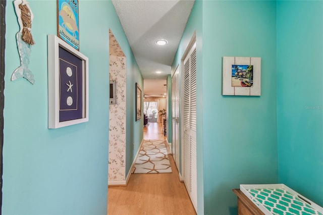 corridor featuring wood finished floors, baseboards, and a textured ceiling