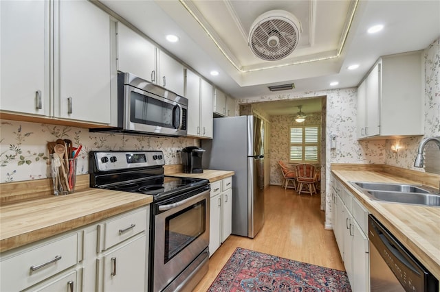 kitchen featuring a sink, a raised ceiling, wood counters, and stainless steel appliances