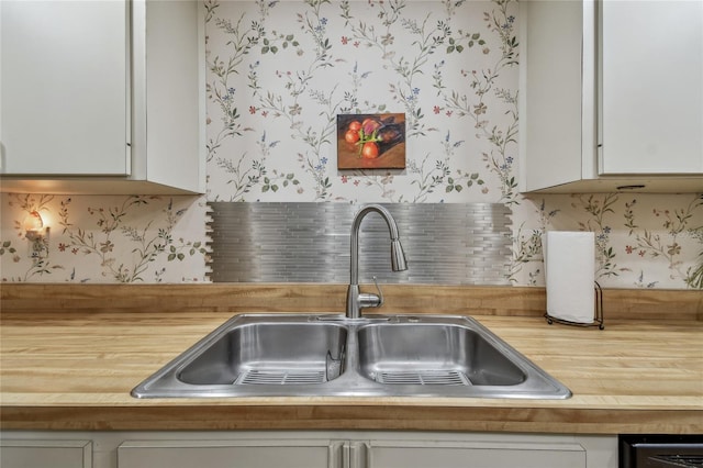 kitchen with a sink, decorative backsplash, wallpapered walls, and white cabinetry