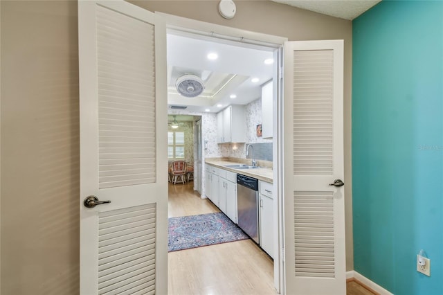 kitchen with a sink, light countertops, white cabinets, dishwasher, and light wood-type flooring