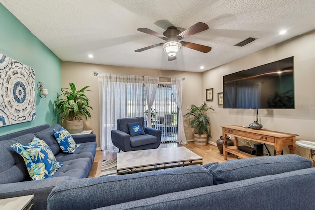 living room featuring ceiling fan, visible vents, a textured ceiling, and wood finished floors