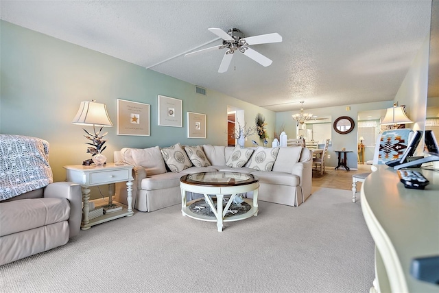 carpeted living room featuring a textured ceiling, ceiling fan with notable chandelier, visible vents, and baseboards